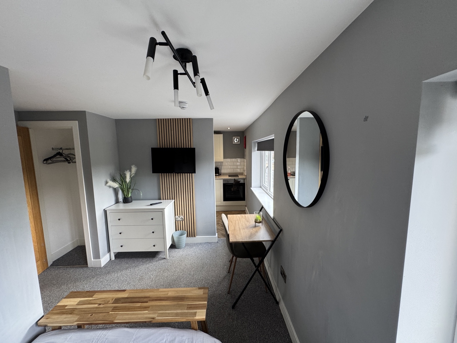 Bedroom with a wall-mounted TV on a slatted wall and a round mirror