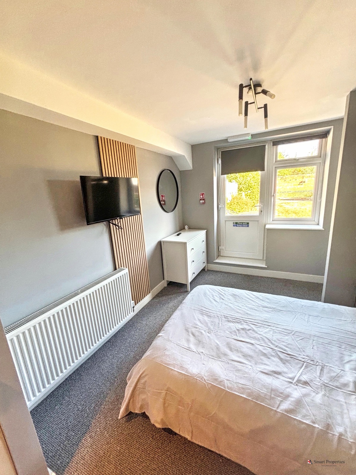 Bedroom with a wall-mounted TV on a slatted wall and a white chest of drawers
